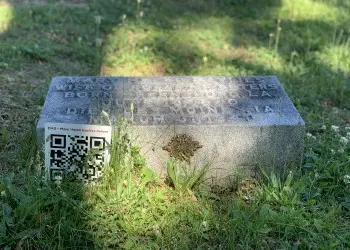 A small, flat square tombstone is accompanied by a sign with a QR code.