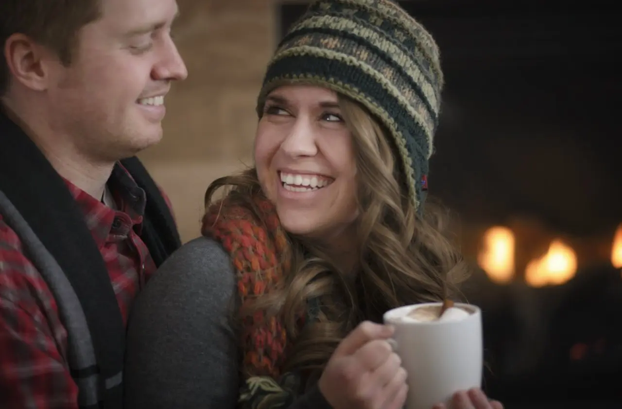 A man and women snuggle while drinking a warm cup of coffee. 