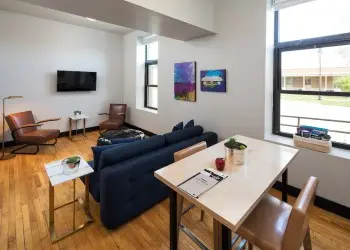 A luxurious hotel room featuring leather chairs, a flat-screen TV, comfortable couch and kitchen table.