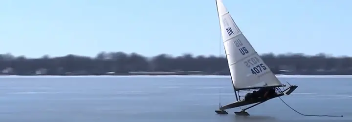 An ice boat races across a frozen lake wile drifting up on one skid. 