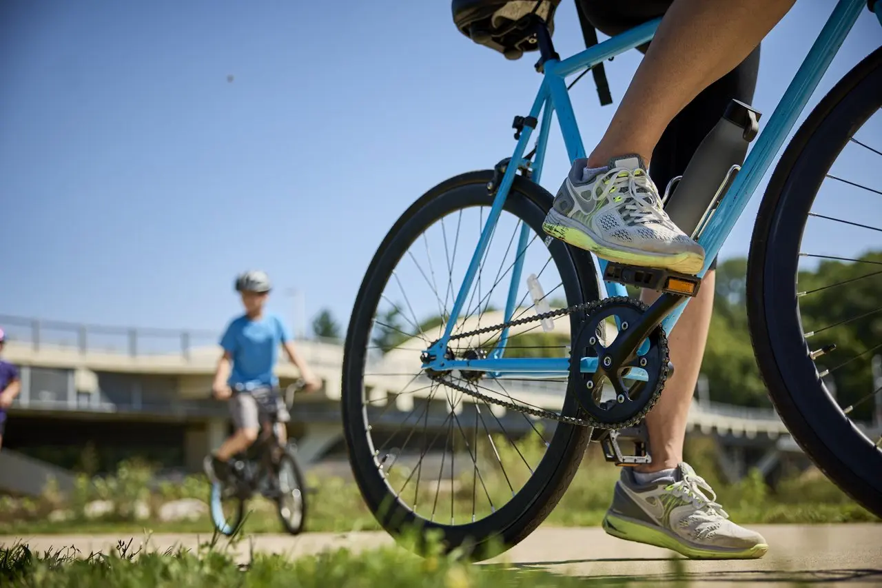 A zoomed in shot of a bike wheel with another biker and a bright blue sky in the background.