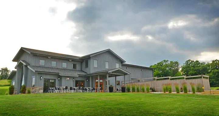 A view of Covered Bridges Winery with seats set up on a patio and lush grass surrounding the building
