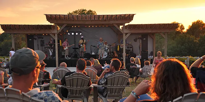 A crowd of people in lawn chairs listen to a band perform outside at Fireside Winery