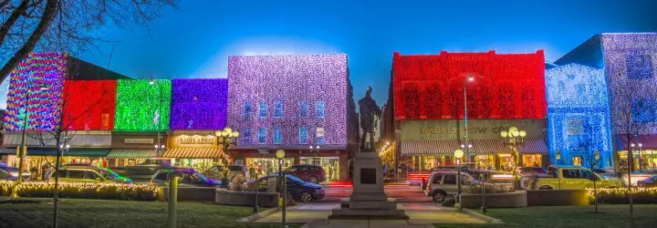 Entire sides of buildings in a town square are covered in bright red, green, blue and purple holiday lights.