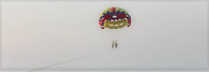 Two riders soar below a colorful parasail high in the sky. 