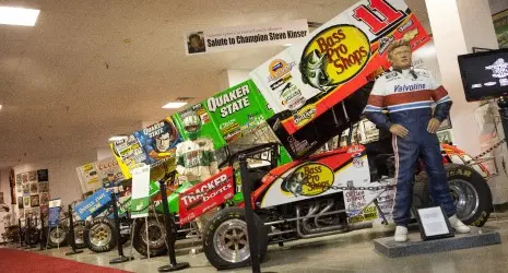 A line of sprint cars lead down a red-carpeted aisle.