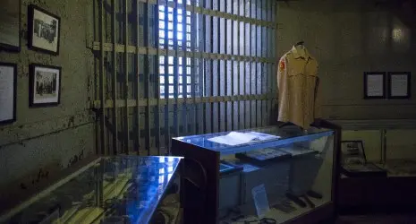 A table displaying prison artifacts and a guard's uniform stand in front of barred windows.