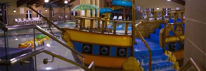 a pirate ship water playground sits before an indoor splash pad and pool. 