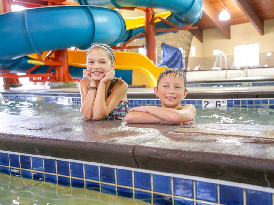 Two children, a girl on the left and boy on the right, smile from the indoor lazy river at Honey Creek Resort.