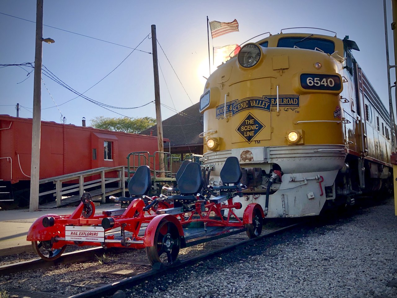 a red four-person rail bike sits in front of a yellow train engine as the sun sets behind them.