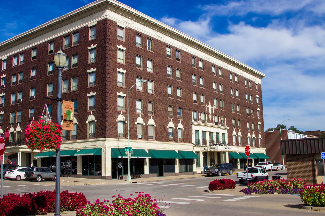 A six story brick building with green awnings sits on a street corner.