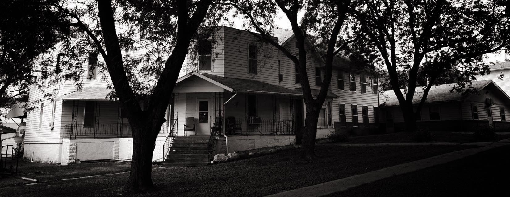 A black and white photo of an old white house surrounded by trees.