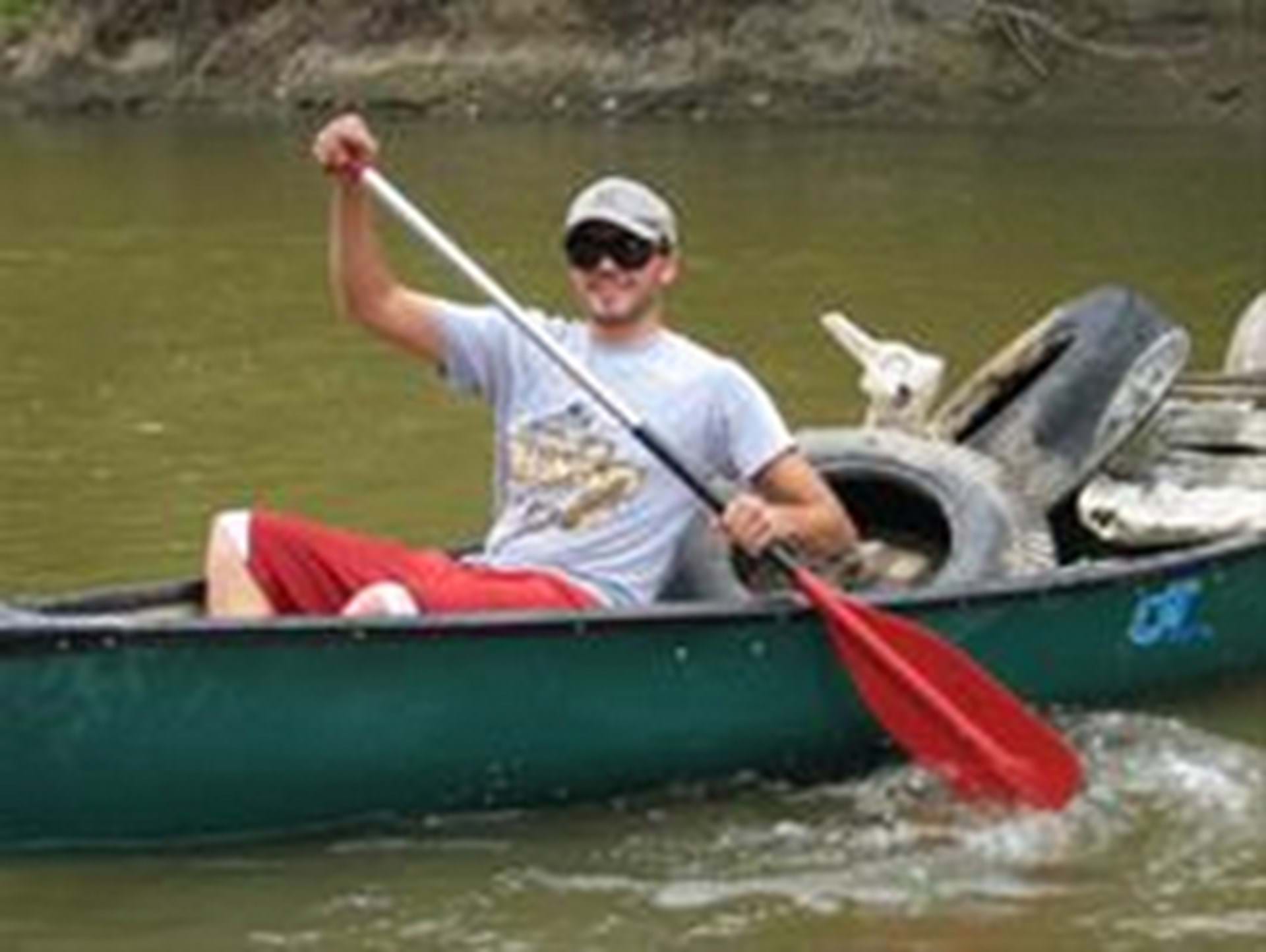 Man paddling canoe with river junk in it