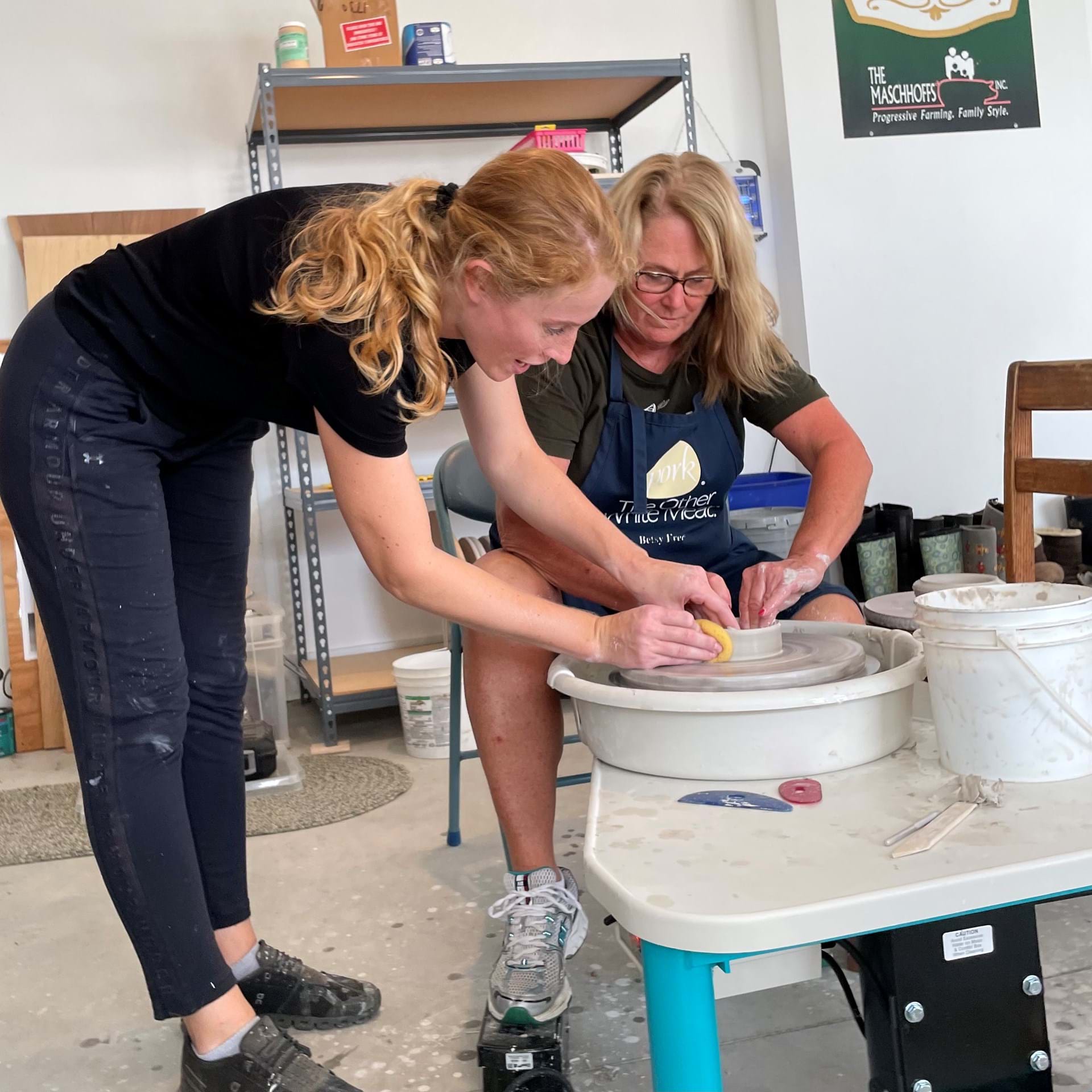 Caroline Freese helping someone throw on the pottery wheel.